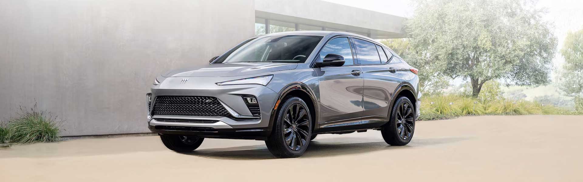 2025 Buick Envista compact SUV in silver parked on a paved driveway with greenery in the background.