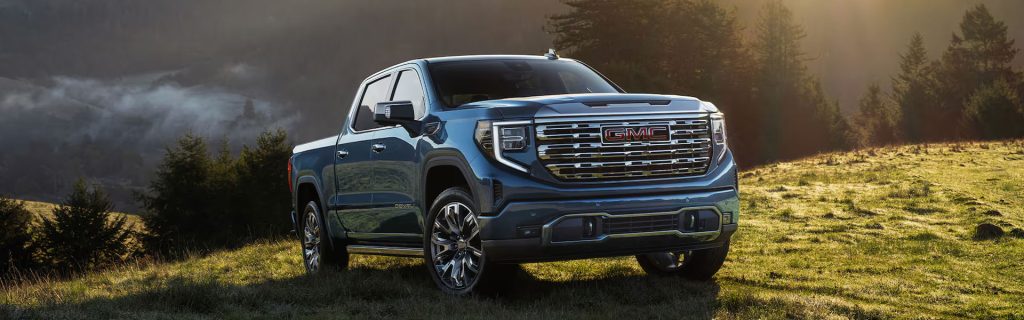 2026 GMC Sierra 1500 truck shown on a scenic hillside at sunset, highlighting bold grille design, premium styling, and powerful capability.