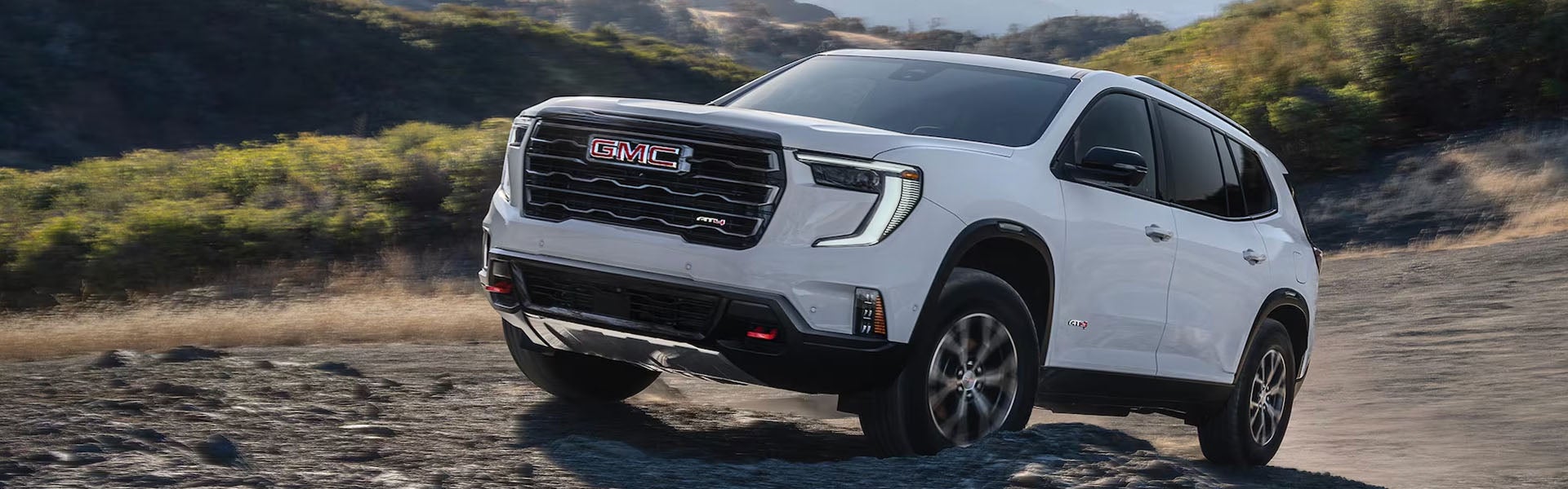 White 2026 GMC Acadia driving up a steep country road