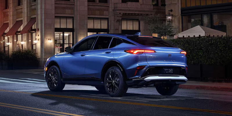 2026 Buick Envista compact SUV driving through a city street at night, featuring sleek styling, LED taillights, and a modern urban backdrop.