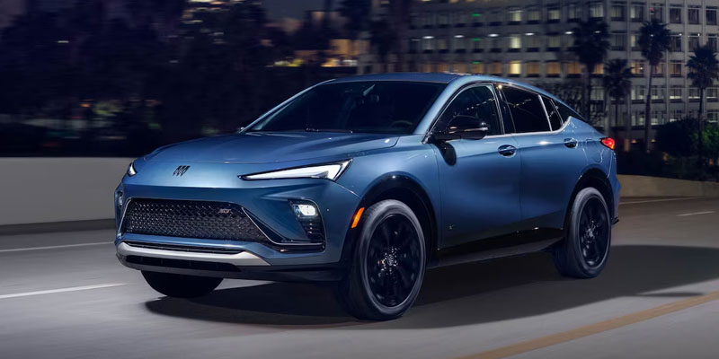 A sleek blue Envista cruises on a city street at night, featuring sharp headlights, a modern grille, and a streamlined design. The scene conveys a sense of sophistication and speed.