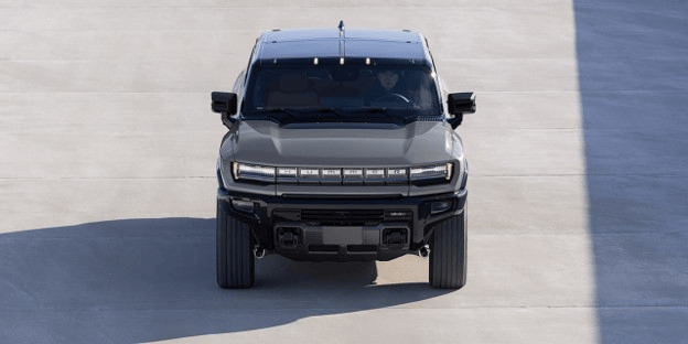 2026 GMC Hummer EV SUV shown from the front on a paved surface, highlighting its wide stance, rugged front design, LED lighting, and distinctive electric SUV styling.